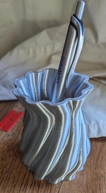 A pencil cup with a flowing organic design.  In a shiny filament, it reflects light in many directions.