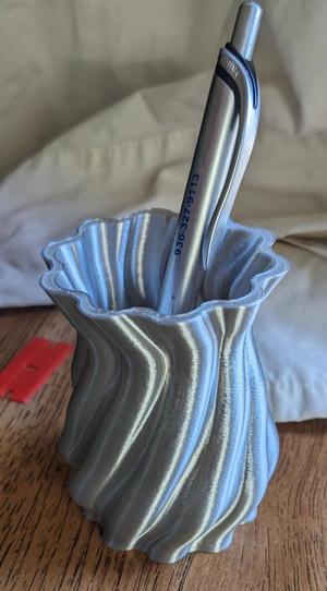 A pencil cup with a flowing organic design.  In a shiny filament, it reflects light in many directions.